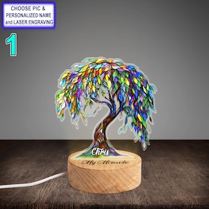 Può includere: Una lampada a forma di albero in vetro colorato con una base in legno. La base è incisa con le parole "Chris My Miracle".