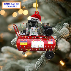 May include: Red air compressor Christmas ornament with a Santa hat that says "Lucas" on it. The ornament is decorated with colorful Christmas lights.