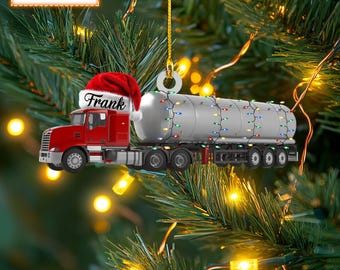 May include: A red and white Christmas ornament shaped like a semi-truck with a tanker trailer. The truck has a Santa hat on the cab and the name "Frank" written on the side. The trailer is decorated with colorful Christmas lights.