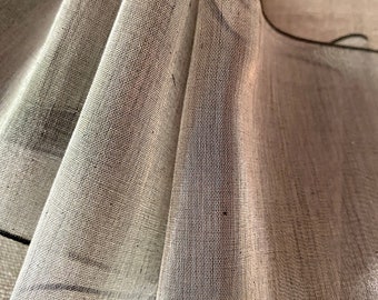 May include: A close-up of a sheer, light gray ribbon with a black edge. The ribbon is folded and ruffled, creating a soft and delicate texture.