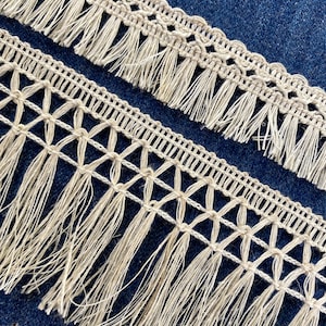 Può includere: Due pezzi di passamaneria beige all'uncinetto con frange. La passamaneria ha un motivo delicato ed è perfetta per aggiungere un tocco di texture ed eleganza a qualsiasi progetto.