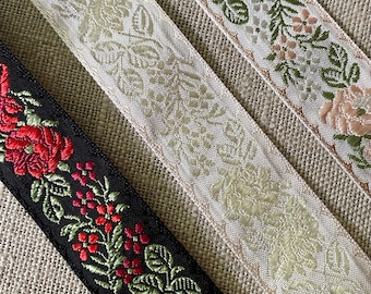 May include: Three different trims of floral patterned ribbon. The first is a cream colored ribbon with a floral pattern. The second is a light pink ribbon with a green floral pattern. The third is a black ribbon with a red floral pattern.