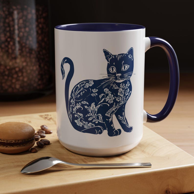 Puede incluir: Taza de cer&aacute;mica blanca con borde y asa azules. La taza presenta una ilustraci&oacute;n azul y blanca de un gato con dise&ntilde;os florales.