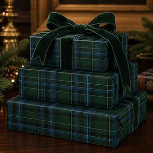 May include: Three rectangular gift boxes stacked vertically, wrapped in dark green and blue plaid paper. The top box is adorned with a large, wide dark green velvet ribbon tied in a bow, featuring long, flowing ends that drape over the sides.