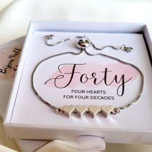 May include: A silver bracelet with four heart charms and a sliding clasp. The bracelet is in a white box with a pink and white card that says "Forty Four Hearts for Four Decades".