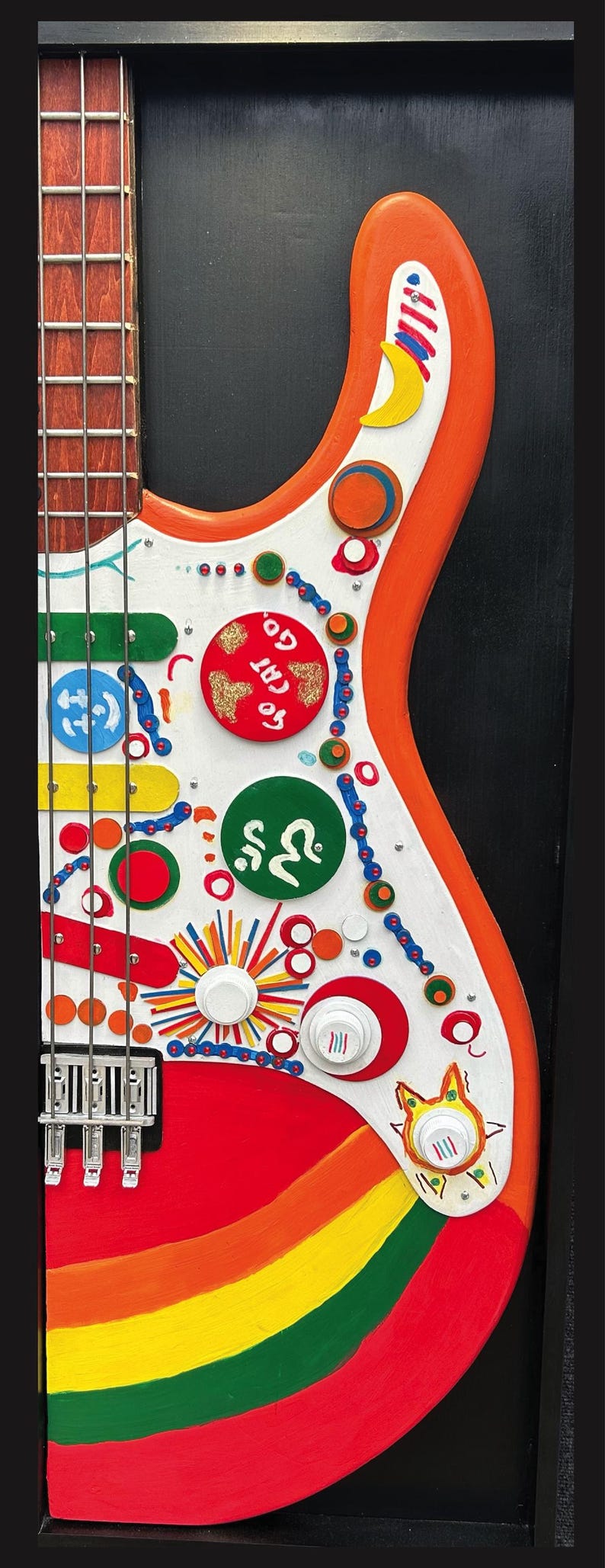 Może przedstawiać: Kolorowa, ręcznie malowana gitara basowa z tęczowym wzorem i r&oacute;żnymi elementami dekoracyjnymi. Gitara ma biały korpus z pomarańczowymi wykończeniami, czerwony pickguard i drewnianą szyjkę. Korpus zdobią koła, linie i napis "GO CAT GO."