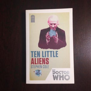 May include: A book cover featuring a man in a dark suit holding a blue object. The title is "Ten Little Aliens" by Stephen Cole. The cover also includes the Doctor Who logo.
