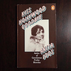 May include: A brown book cover with the title "Kiss Hollywood Goodbye" in pink and blue letters. The author is Anita Loos, author of "Gentlemen Prefer Blondes". A black and white photo of a woman with short dark hair is on the cover.
