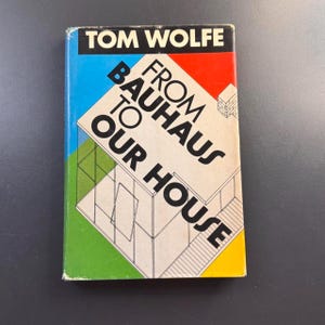May include: A hardcover book titled "From Bauhaus to Our House" by Tom Wolfe. The cover features a colorful design with blue, red, green, and yellow blocks. The title is in bold, black font, with an architectural illustration.