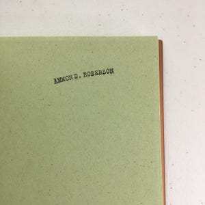 May include: A green book with the name "AMMON D. ROBERSON" printed on the cover.