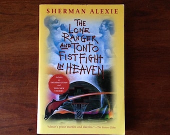 May include: A yellow paperback book with a colorful illustration of a basketball hoop and a salmon jumping through the air. The book title is "The Lone Ranger and Tonto Fist Fight in Heaven" by Sherman Alexie. It includes an introduction and two new stories.