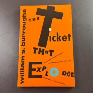 May include: A book cover with an orange background and black and white text. The title "The Ticket That Exploded" is prominently displayed. The author's name, William S. Burroughs, is printed vertically on the left side.