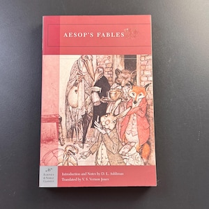 May include: A paperback book titled Aesop's Fables with a red and white cover. The cover features a detailed black and white illustration of anthropomorphic animals including a fox, rabbit, and bird. The Barnes & Noble Classics logo is visible.