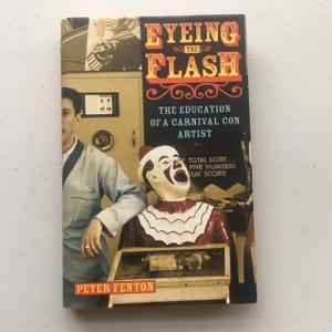 May include: A book cover with a red, white, and blue clown face and the title "Eyeing the Flash: The Education of a Carnival Con Artist" by Peter Fenton.
