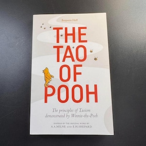May include: A book titled "The Tao of Pooh" by Benjamin Hoff. The cover features large red text and a yellow illustration of Winnie-the-Pooh. The book's subtitle reads "The principles of Taoism demonstrated by Winnie-the-Pooh."