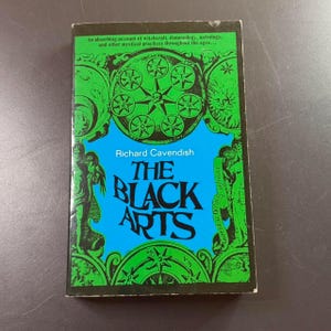 Może przedstawiać: Zabytkowa książka zatytułowana "The Black Arts" autorstwa Richarda Cavendisha. Okładka ma niebieskie tło z zielonymi, ozdobnymi wzorami i tekstem. Tytuł książki jest dużymi, pogrubionymi literami. Okładka zawiera r&oacute;wnież tekst o czarach i mistycyzmie.
