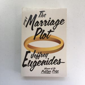 May include: The Marriage Plot, a novel by Jeffrey Eugenides, winner of the Pulitzer Prize. The cover features a gold ring with a white background.