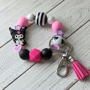 Pulsera con forma de conejito diablo japonés en color rosa y negro con dije de silicona que se estira hasta 7,5" y se puede llevar con llavero y borla