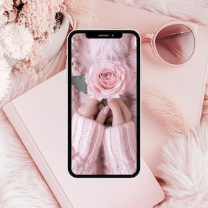 May include: A pink rose held in hands wearing a pink knitted sweater. The phone screen is a close-up of the rose and hands.