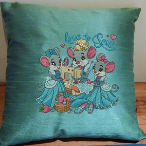 May include: A teal blue pillow with embroidered mice sewing on a sewing machine. The pillow has the text "Love to Sew" embroidered on it.