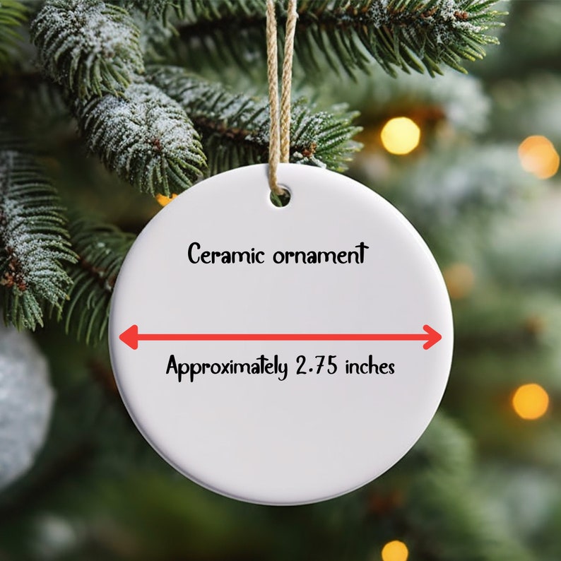 May include: A white ceramic ornament with the text "Ceramic ornament" and "Approximately 2.75 inches". The ornament is round and hangs from a beige string. The background is a blurred Christmas tree.