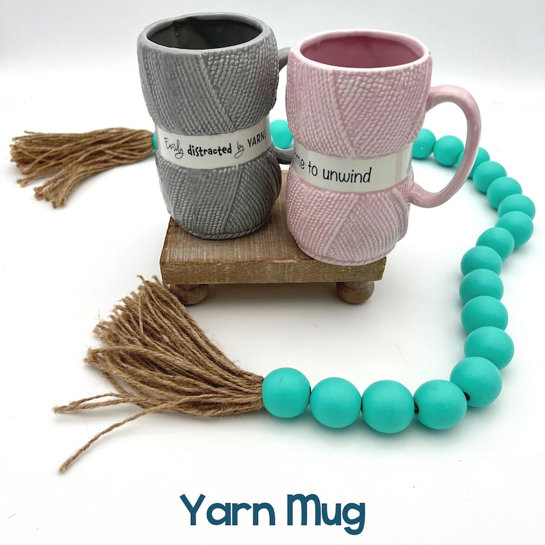 two yarn mugs are shown on a wooden riser.
