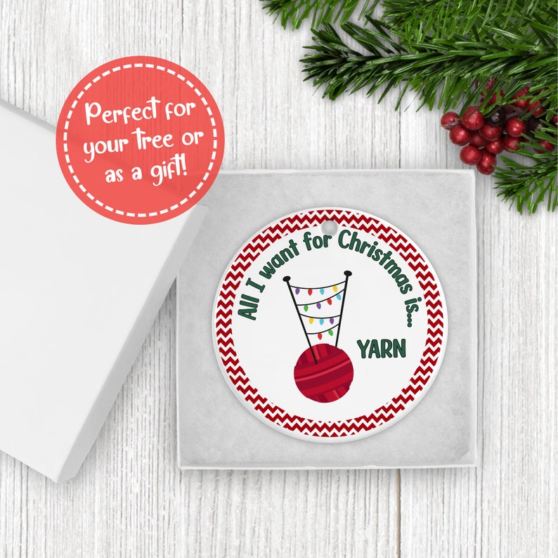 A knitting Christmas ornament is shown in a gift box near greenery.