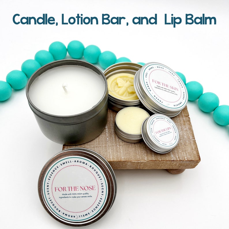 May include: A set of three small tin containers with labels that read "For the Nose", "For the Skin", and "For the Lips". The containers are filled with white and yellow creams. A teal blue beaded necklace is in the background. A white candle is in a silver tin container.