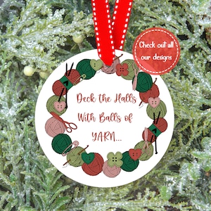 May include: White round Christmas ornament with a green, red, and pink yarn ball wreath and the text "Deck the Halls With Balls of YARN..."