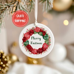 May include: White ceramic Christmas ornament with a wreath of red and green yarn balls and the text "Merry Knitmas".