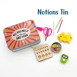 May include: A metal tin with a colorful design that says "All you need is love and yarn". The tin is filled with various knitting and crocheting notions, including scissors, needles, stitch markers, a yarn counter, and a gauge ruler.