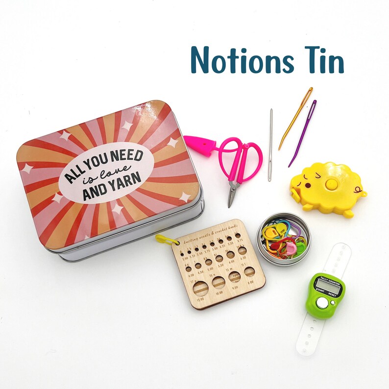 May include: A metal tin with a colorful design that says "All you need is love and yarn". The tin is filled with various knitting and crocheting notions, including scissors, needles, stitch markers, a yarn counter, and a gauge ruler.