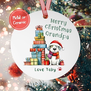 May include: White round Christmas ornament with a cartoon dog wearing a Santa hat and scarf, surrounded by a stack of colorful presents. The ornament reads "Merry Christmas Grandpa" and "Love Toby".
