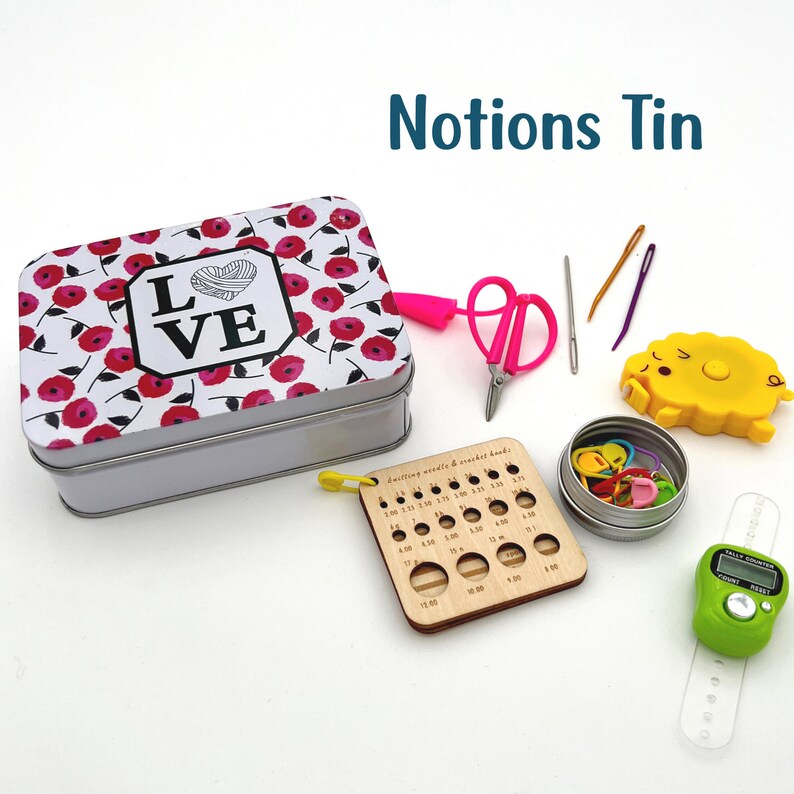 Notions tin with love and floral design.  On the white background are items included in the notions tin:  scissors, needles, stitch markers, stitch counter.
