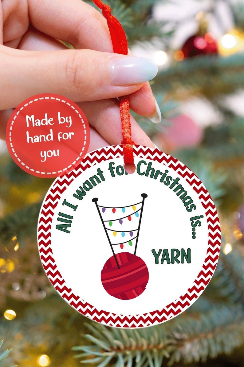 May include: Round Christmas ornament with a red ribbon. The ornament features a red yarn ball, a knitting needle design with colorful lights, and the text "All I want for Christmas is... YARN."