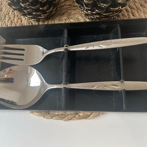 May include: A silver serving set with a fork and spoon in a black velvet box. The box has the text "Community Stainless by Oneida" on the front.