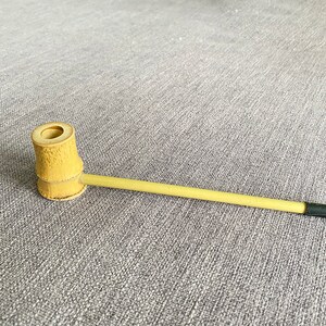 May include: A natural bamboo smoking pipe with a round bowl and a long, thin stem.