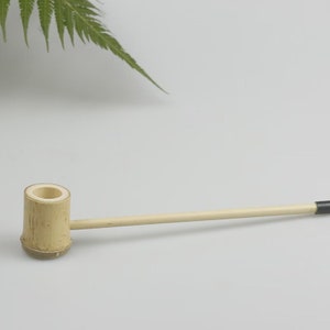May include: A simple, natural bamboo smoking pipe with a black mouthpiece. The pipe is about 10 inches long and has a round bowl.