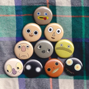 May include: Nine round buttons with various cartoon faces. The buttons are colourful and feature different expressions, including smiling, frowning, and surprised.