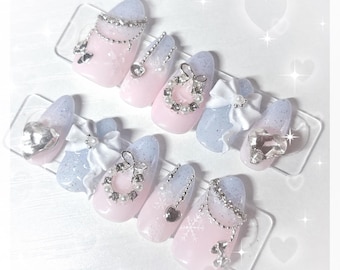 Peut inclure: Ensemble de faux ongles avec un dégradé rose clair et bleu. Chaque ongle est orné d'éléments décoratifs tels que des strass, des perles, des nœuds et des breloques en forme de cœur. Certains ongles présentent des motifs de flocons de neige.
