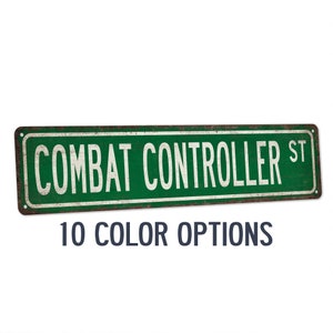 May include: A green metal sign with the text "COMBAT CONTROLLER ST" in white lettering. The sign has a distressed, rusty look. 10 COLOR OPTIONS is written in blue below the sign.