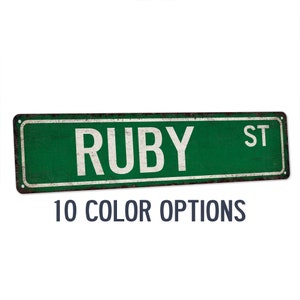 May include: A green metal street sign with the text "RUBY ST" in white lettering. The sign has a distressed, rusty look. The text "10 COLOR OPTIONS" is printed below the sign.