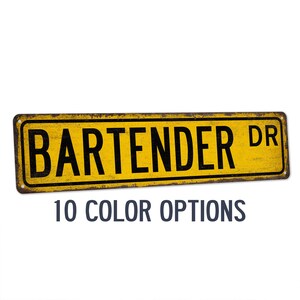 May include: Yellow metal sign with the text "BARTENDER DR" in black lettering. The sign has a distressed, vintage look. 10 color options are available.