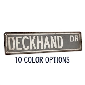 May include: A rustic metal sign with the text "DECKHAND DR" in white lettering on a gray background. The sign has a distressed, weathered look and is perfect for adding a touch of vintage charm to your home decor.