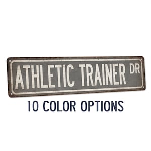 May include: A rustic metal sign with the text "ATHLETIC TRAINER DR" in white lettering on a gray background. The sign has a distressed, aged look and is available in 10 color options.
