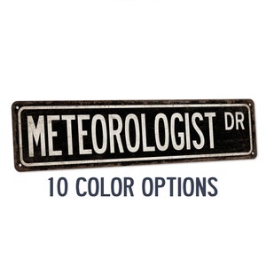 May include: A rustic metal sign with the text "METEOROLOGIST DR" in white lettering on a black background. The sign has a distressed, aged look and is perfect for a home or office.