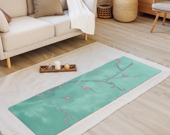 May include: A green yoga mat with a floral design featuring pink blossoms and branches. The mat is laid out on a white rug in a living room setting.