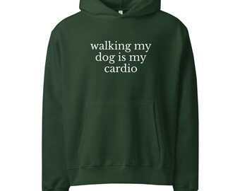Puede incluir: Una sudadera con capucha verde oscuro con un bolsillo delantero y una capucha. El texto blanco en la parte delantera dice "walking my dog is my cardio". Esta sudadera es una prenda cómoda e informal.