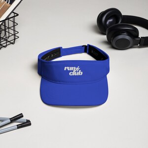 May include: A royal blue visor with a white embroidered logo that says "run club" in a retro font.