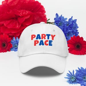 May include: White baseball cap with the text "PARTY PACE" in red and blue block letters. The hat is surrounded by red and blue flowers.